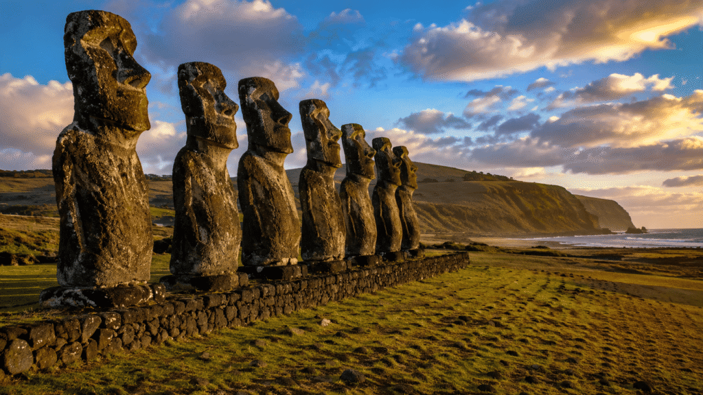 Moais gigantes da Ilha de Páscoa no Chile alinhados em paisagem natural de Rapa Nui com oceano ao fundo e iluminação dourada de fim de tarde.